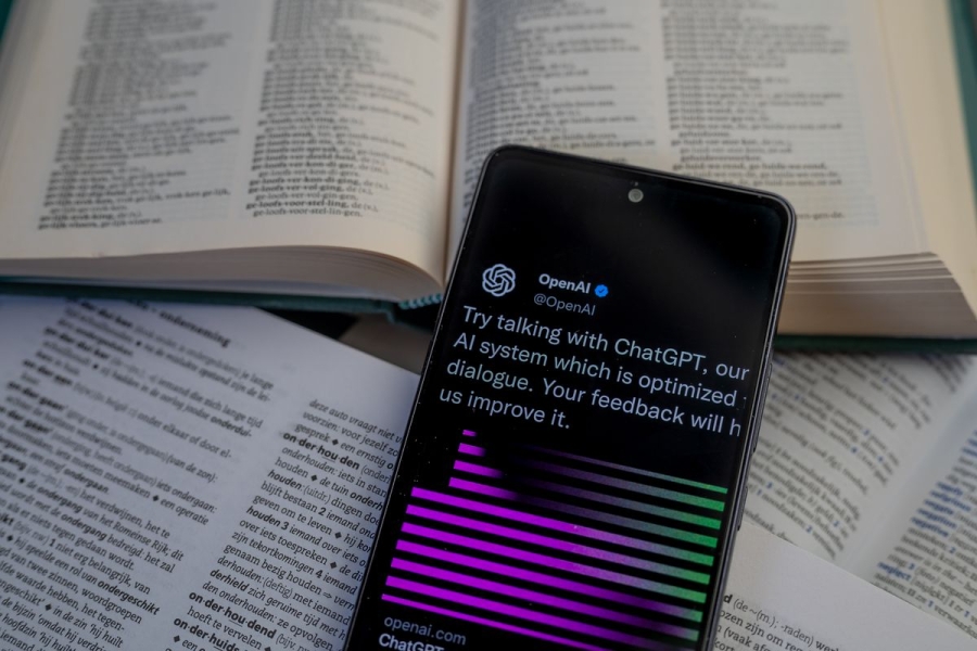A cellphone displaying an OpenAI page while propped atop open printed books.