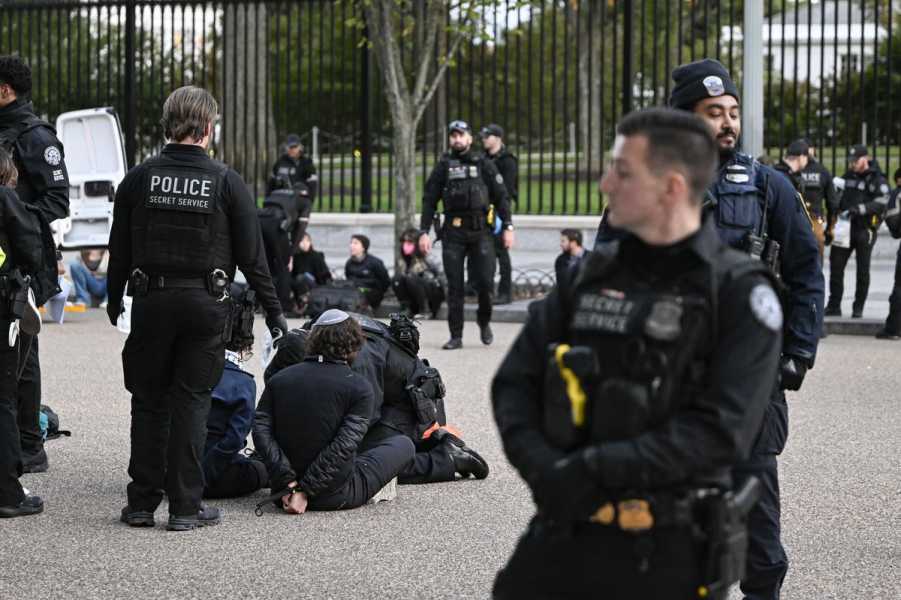 Uniformed police officers wearing all black stand above protestors, who are seated on the ground with their hands cuffed behind their backs, on October 16, 2023, in Washington, DC. 