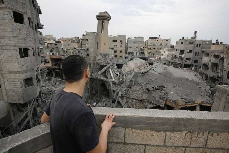 A man stands on a balcony overlooking the destroyed mosque. His back is to the camera.