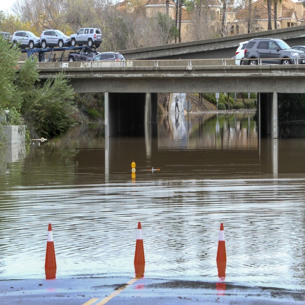 Cars drive over a road flooded by the San Diego River after heavy rains in San Diego, California, on January 7, 2016.