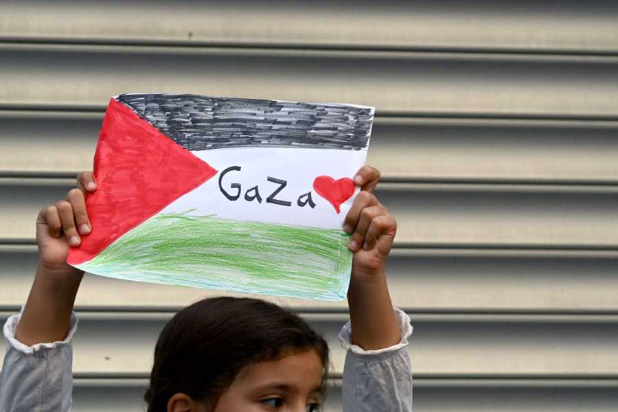 A girl holds a Palestinian flag drawn in marker on white paper. It reads Gaza with a drawing of a heart.