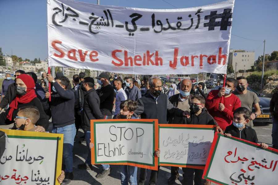 A parade of people: two men hold a large white banner with a hashtag in Arabic; an English message reads: “Save Sheikh Jarrah.” In front of the crowd are children holding signs, some in English: “Stop ethnic cleansing” and some in Arabic.