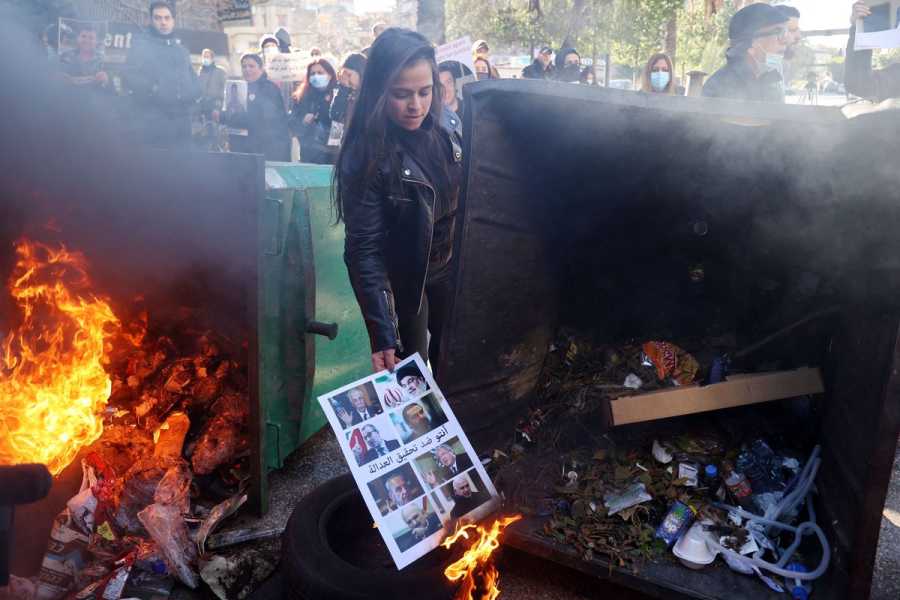 The protester, a woman with long dark hair and a leather jacket, bends to let her poster catch the flames rising from an overturned garbage bin. Among its faces is an Arabic slogan that reads: “You are against achieving justice.”