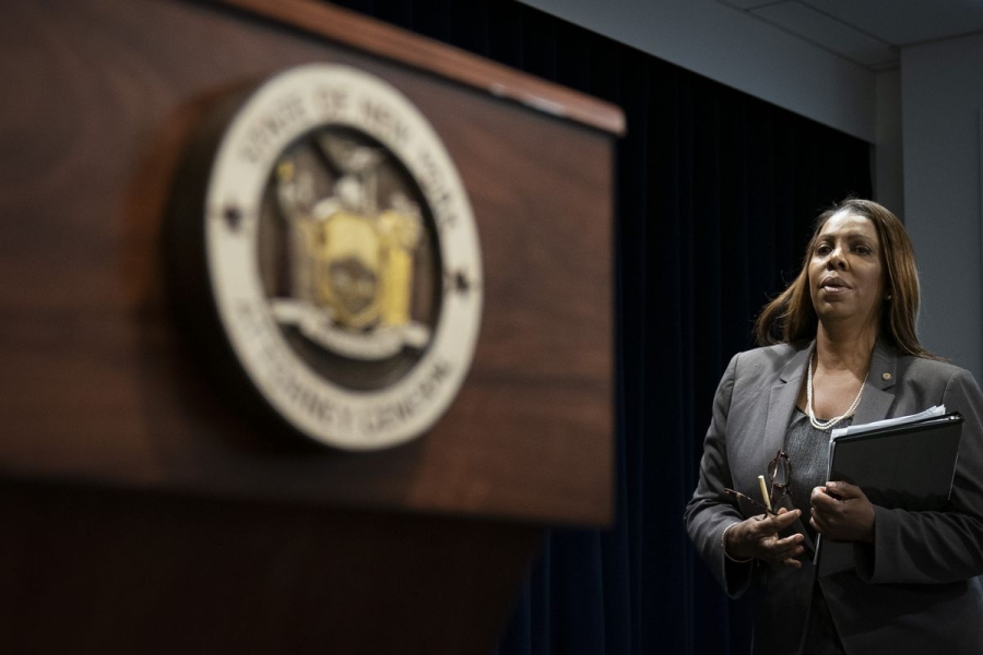 New York Attorney General Letitia James stands next to the state seal while holding a binder.