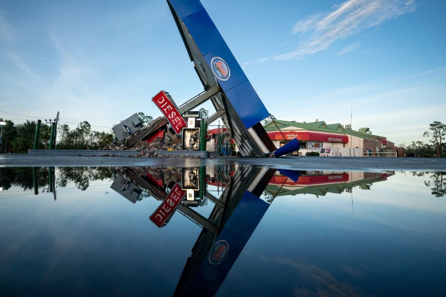 A gas station is tipped on its side into standing water, as the surrounding area is flooded.