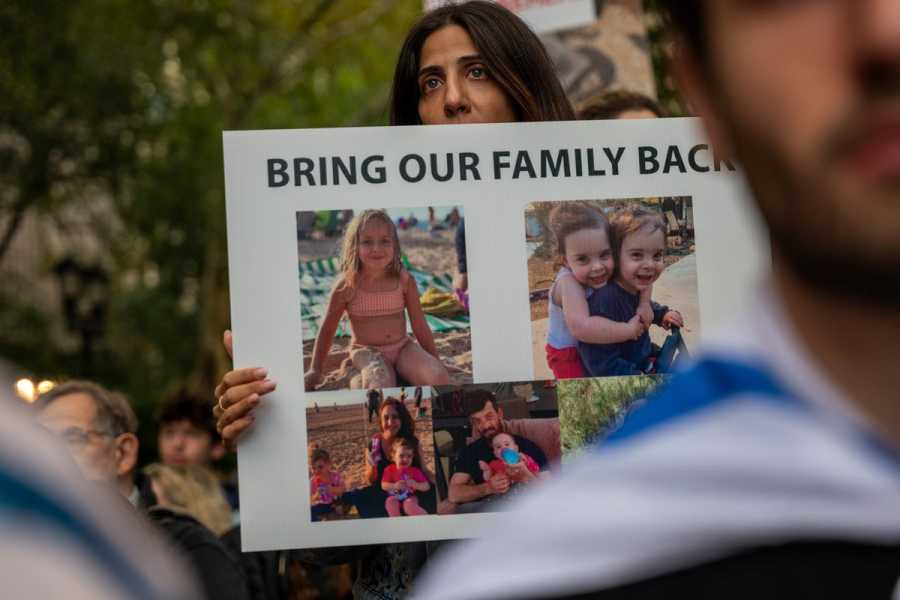 A woman holds a poster featuring images of children, with the words “Bring Our Family Back” printed across the top. 