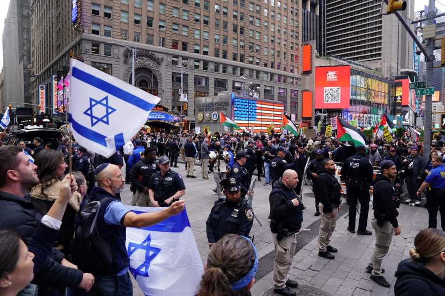 A crowd of people waving Israeli flags face another crowd waving Palestinian flags, separated by New York City police officers.