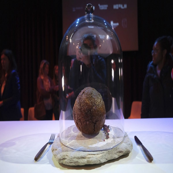 A very large meatball is seen on a table under a glass food dome.