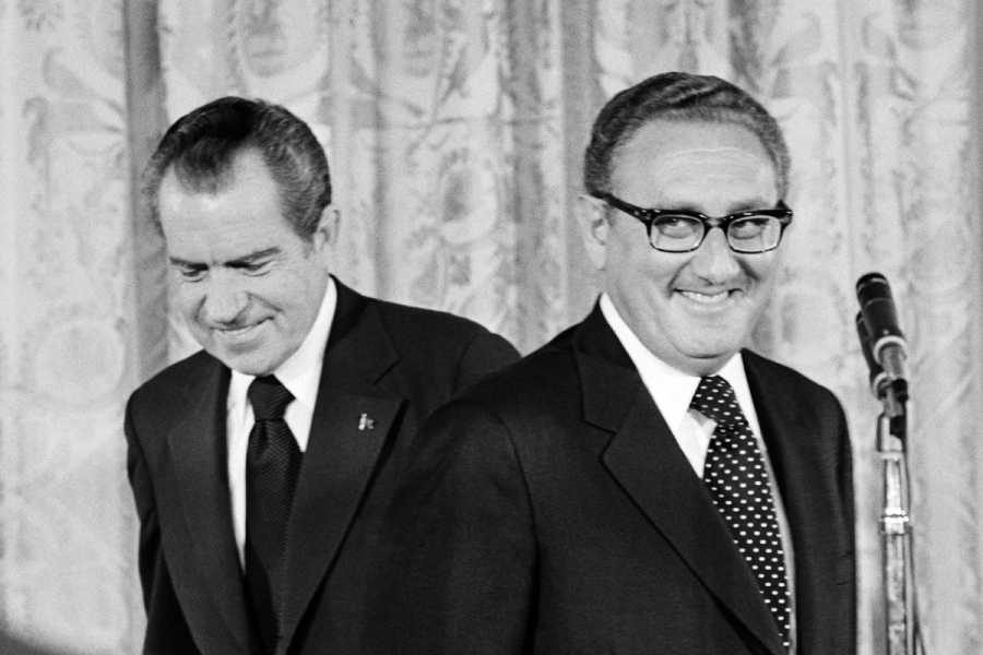 A black-and-white photo shows Nixon on the left with Kissinger on the right, both smiling with a microphone in the background.