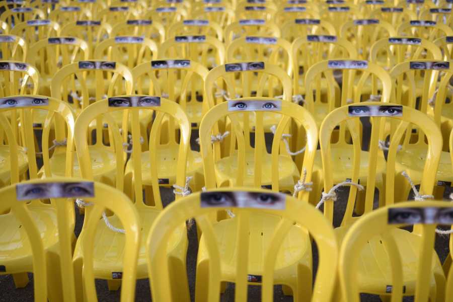  Rows of yellow chairs, each with images of a person’s eyes pasted to the top.