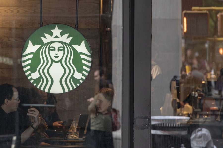 A Starbucks coffee shop in New York seen from outside. There’s a logo on the window and a crowd of people sitting inside.