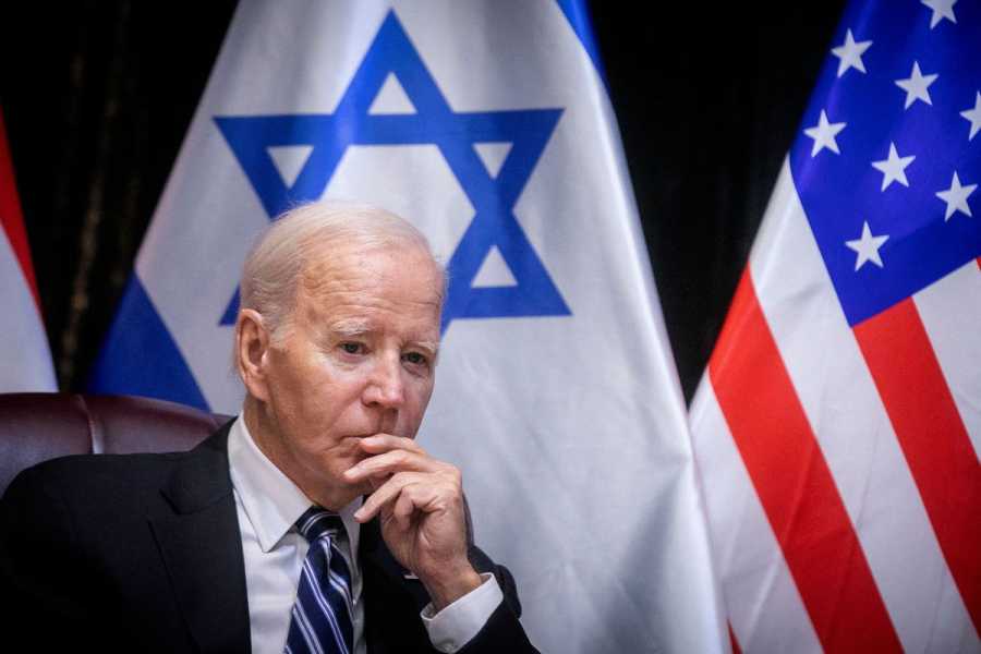 Biden sits in front of an Israel flag with a concerned look on his face.