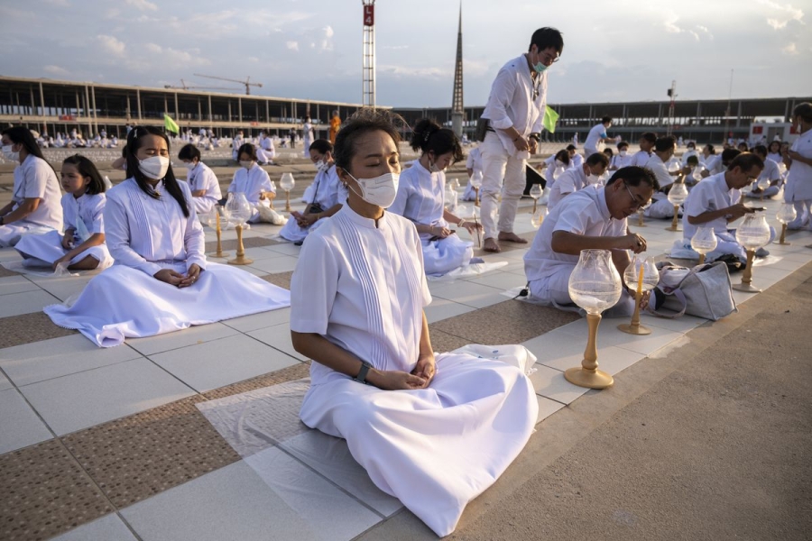 Buddhist devotees wearing white sit and meditate in a large open courtyard.