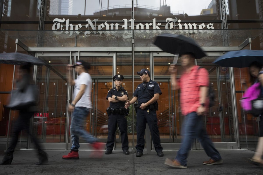Police officers stand in front of the headquarters of the New York Times on June 28, 2018, in New York City. Pedestrians with umbrellas walk by.