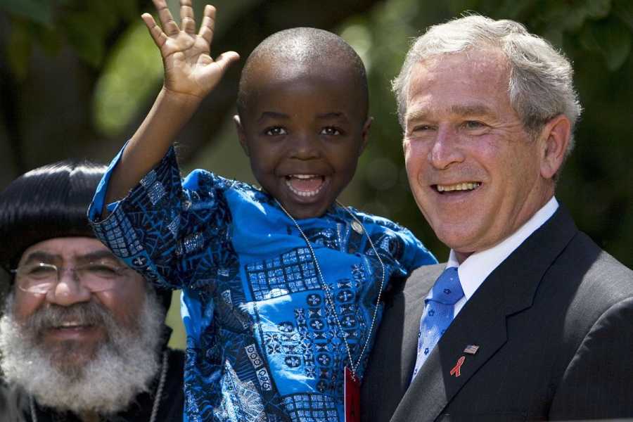 George W Bush holding a waving child, with Bishop Paul Yowakim seen at left. 