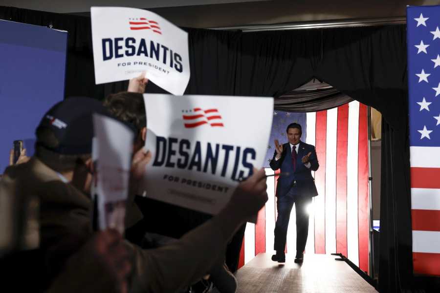 People wave DeSantis signs as Florida Gov. Ron DeSantis enters the room.