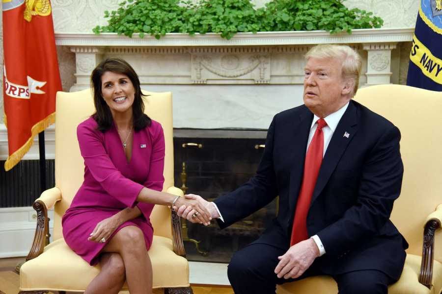 Nikki Haley, smiling into the camera, shakes hands with a distracted-looking Donald Trump.