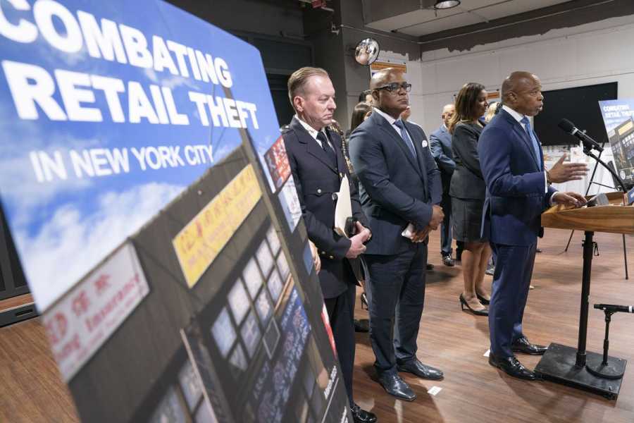 Sigh that reads “Combating Retail Theft” is seen in the foreground while New York City Mayor Eric Adams speaks at a lectern.