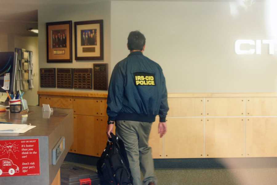 A person wearing an IRS police jacket walks through a house.