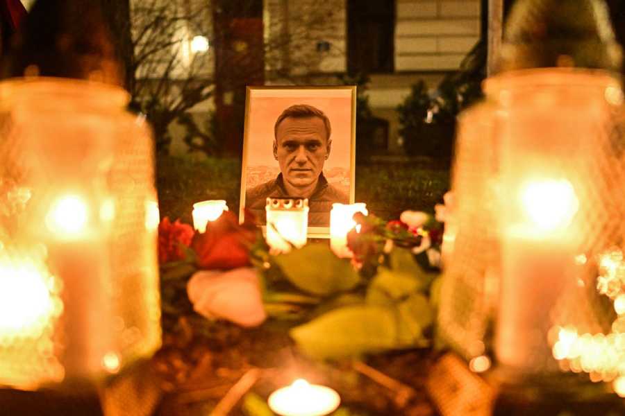 A photo of a row of yellow candles in glass jars; at the end, surrounded by roses, is a color photo of Navalny, a clean-shaven white man with sandy brown hair.