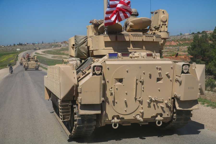 An armored vehicle flying an American flag traveling down a desert road.