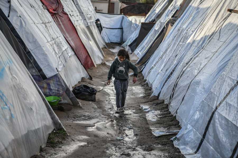 A child walks over muddy ground between rows of tents.