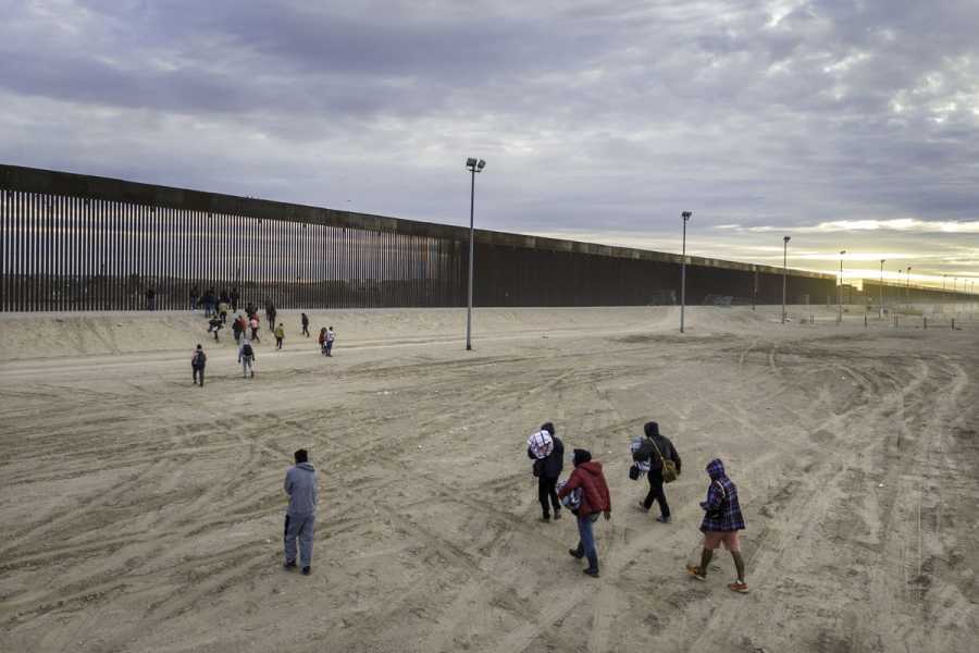 Migrants, viewed from above, walk toward the border wall
