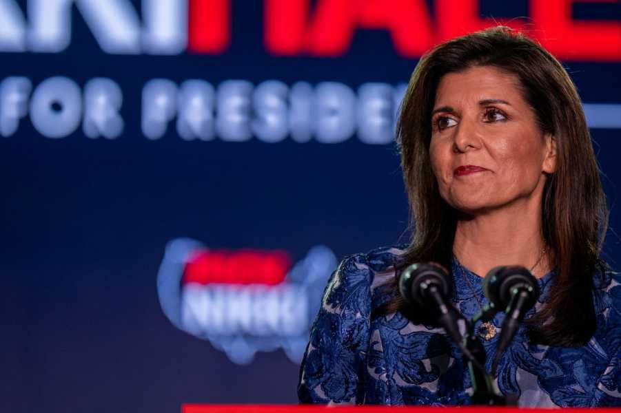 Nikki Haley, wearing a blue embroidered top, stands before a microphone.