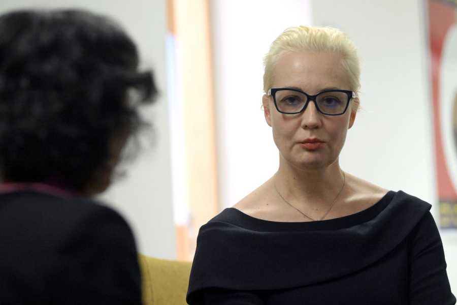 A blonde woman in black with black-framed glasses.