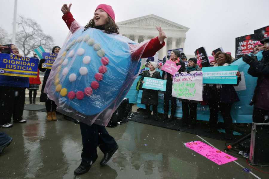 A protester dressed as a pack of birth control pills dances in front of the US Supreme Court, encircled by other protestors holding colorful signs, on March 25 in Washington, DC.