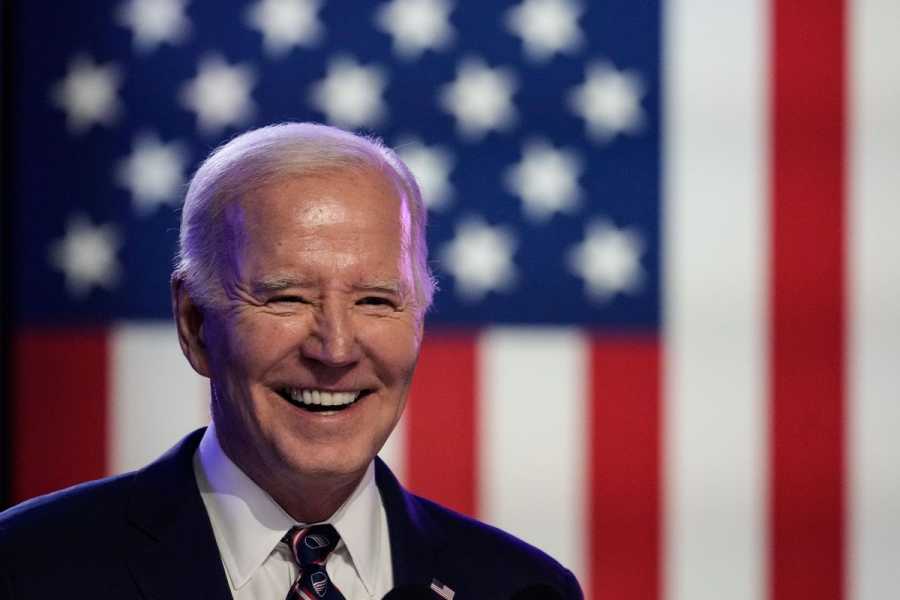 President Biden smiling happily in front of an American flag backdrop.