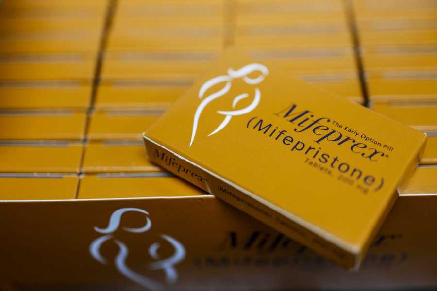 Orange-brown packets of mifepristone tablets neatly arranged, each with a logo of a female figure sketched in white lines. 