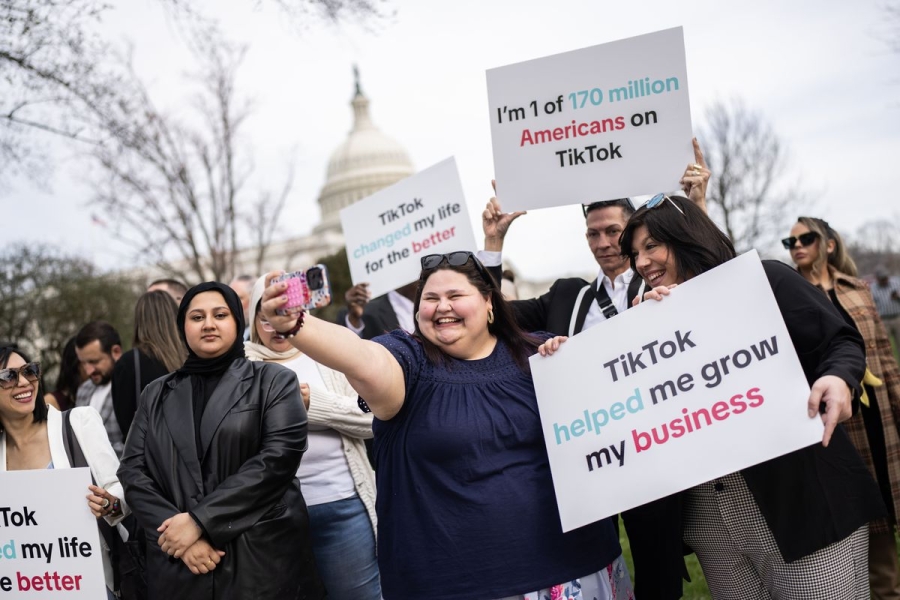 A photograph of TikTok supporters standing outside the US Capitol. They are holding signs supportive of TikTok, reading “TikTok Helped Me Grow My Business” and other similar messages. One supporter is taking a selfie and smiling.
