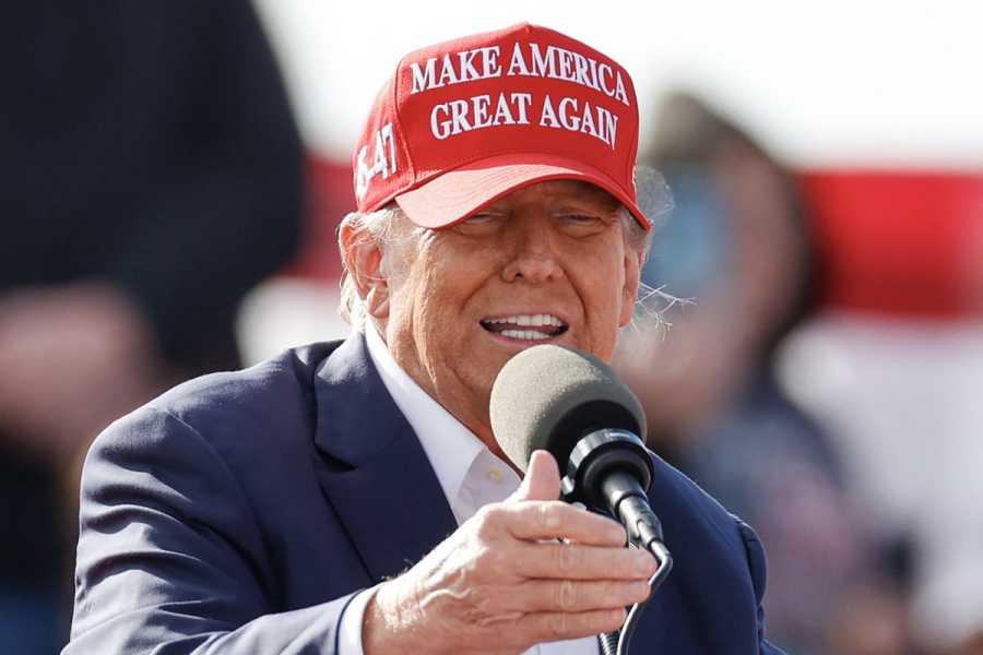 Donald Trump speaking into a microphone while wearing a red “Make America Great Again” hat.