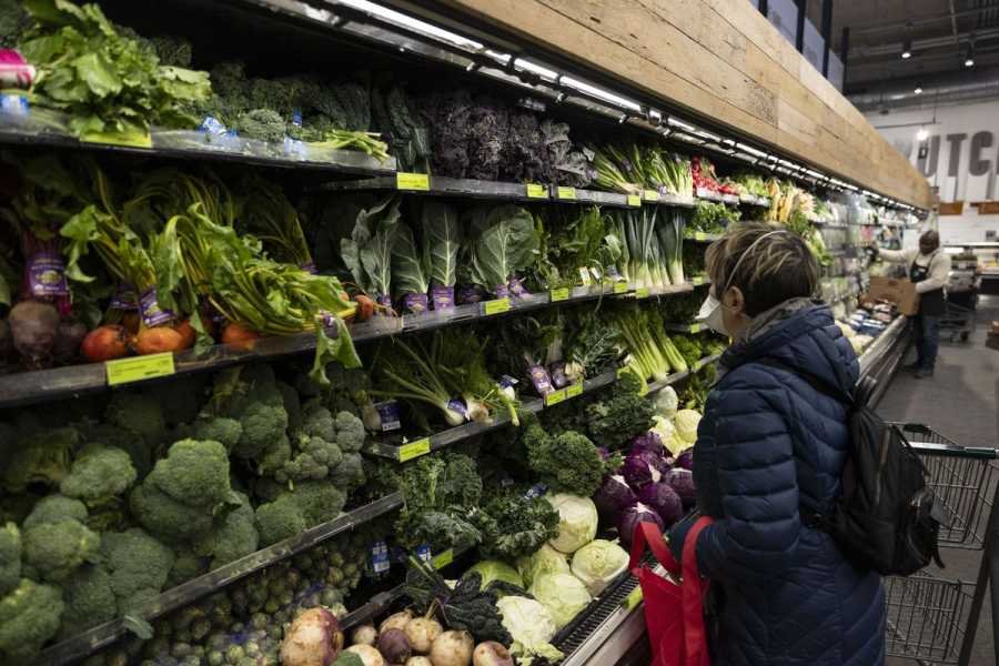 Rows of green vegetables and other produce stretch along an aisle at a Washington, DC, grocery store in February 2024. A shopper with a grocery cart is looking at the produce.