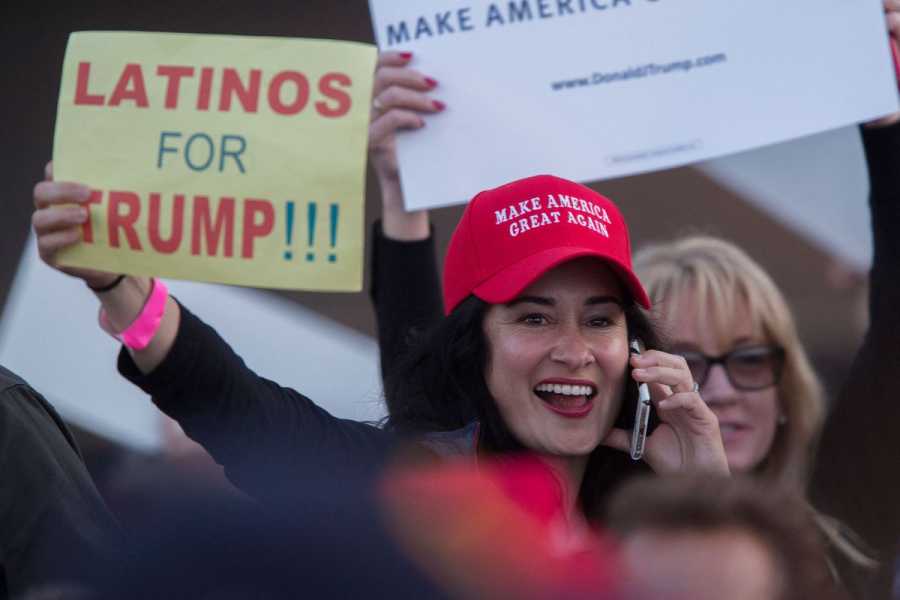 A woman in a MAGA hat holds a sign that says “Latinos for Trump!!!”