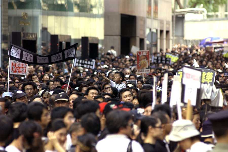 A large crowd of people fill a street, holding banners and signs.