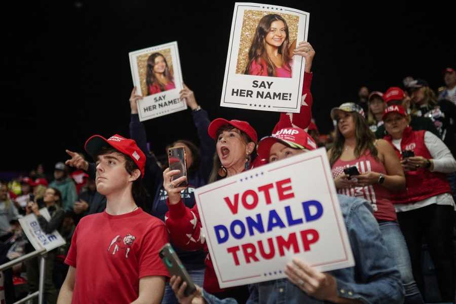A crowd of people wearing red pro-Trump campaign shirts and hats hold photos of Laken Riley printed with the words “SAY HER NAME” and a sign saying “VOTE DONALD TRUMP.”