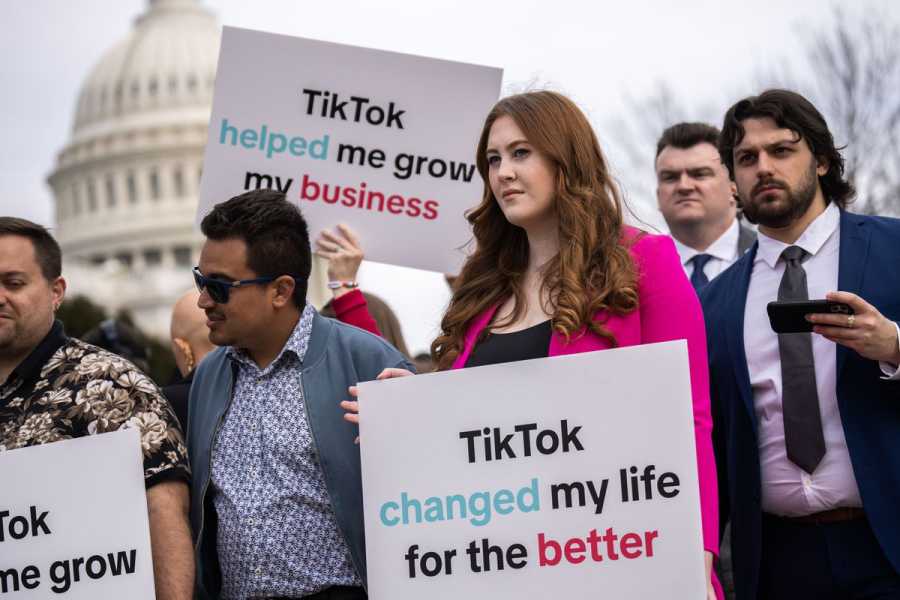A woman in a group of protesters holds up a sign that reads “ TikTok changed my life for the better,” while another sign is visible behind her reading “TikTok helped me grow my business.” The US Capitol is visible behind the group.