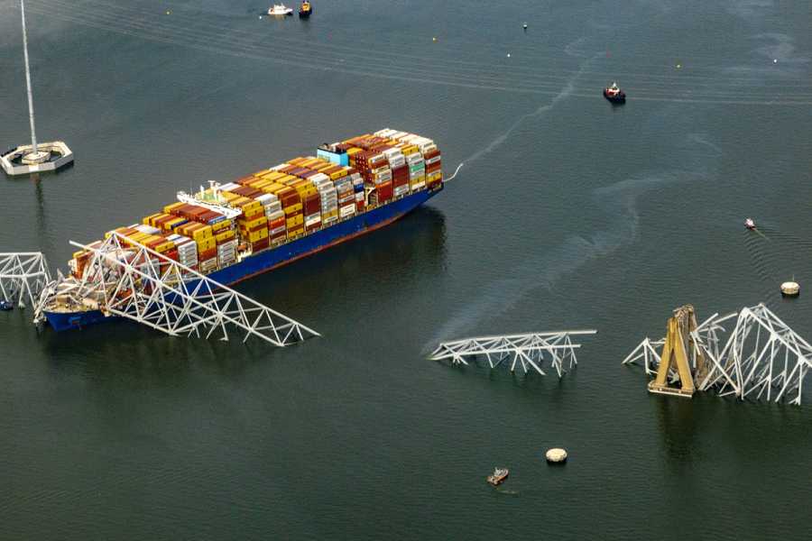 A massive cargo ship sits in a wide river, with a steel bridge span collapsed over and around it.