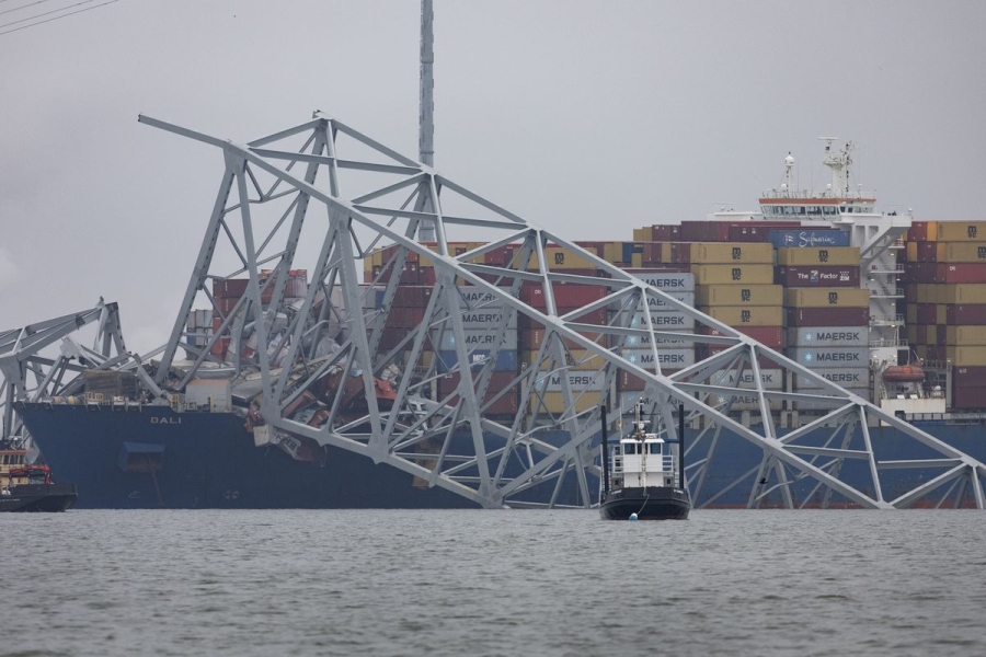 A cargo ship in the water with a piece of a bridge broken across its bow.