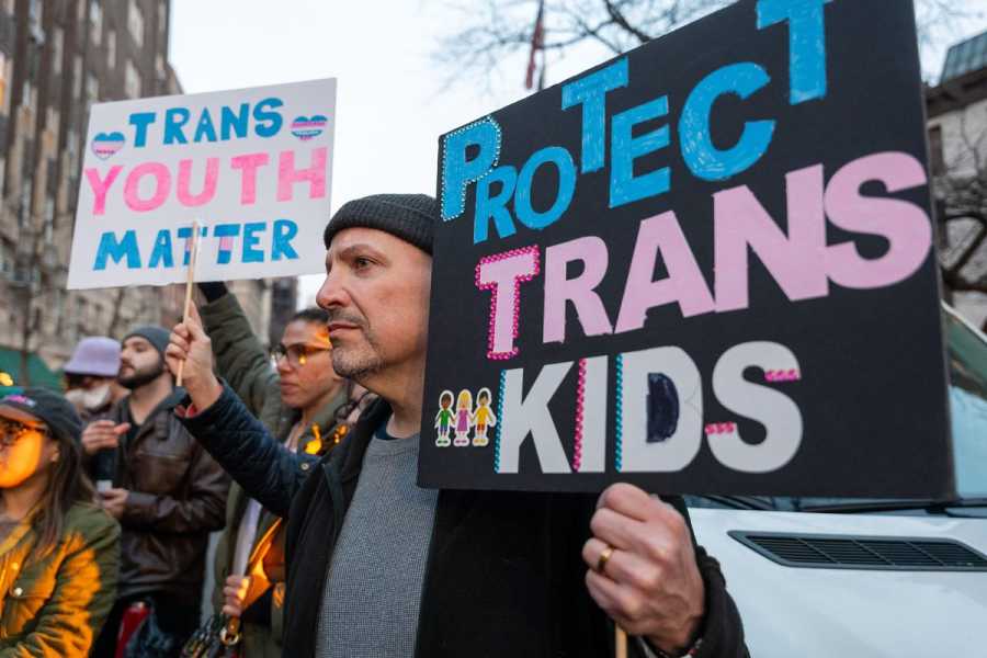 People at a memorial hold signs that say “Trans youth matter” and “Protect trans kids.”
