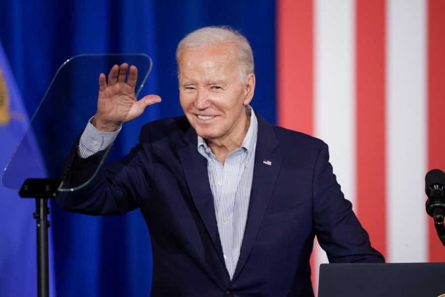 Biden smiles and waves onstage in front of a red, white, and blue backdrop.