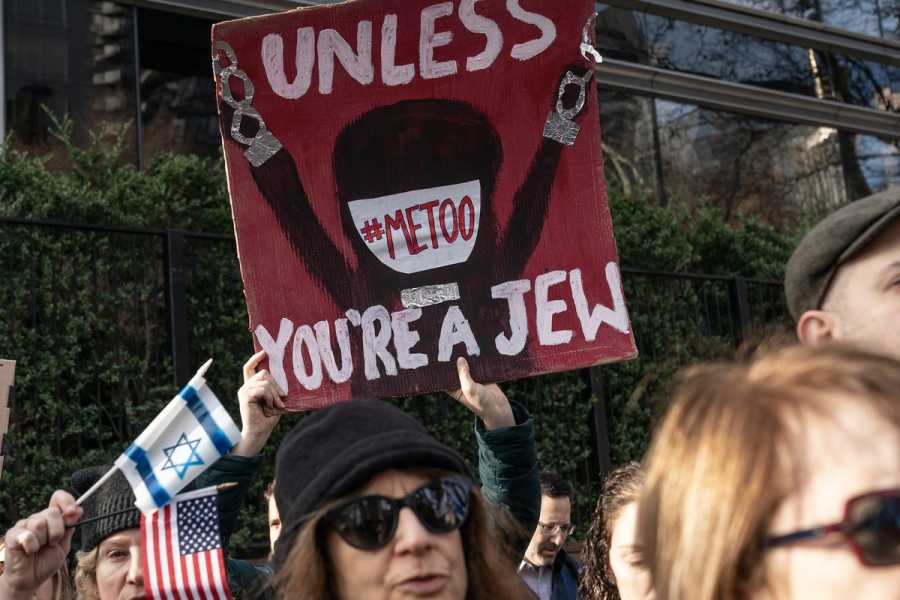 An activist in a swarm of people holds a sign that says “#MeToo unless you’re a Jew.”