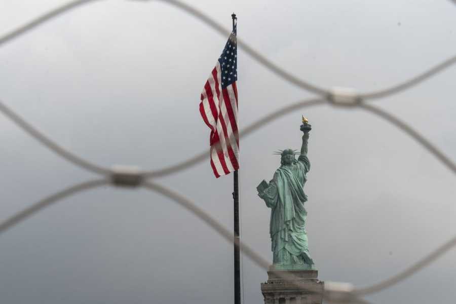 The Statue of Liberty and an American flag, photographed through wire fencing.