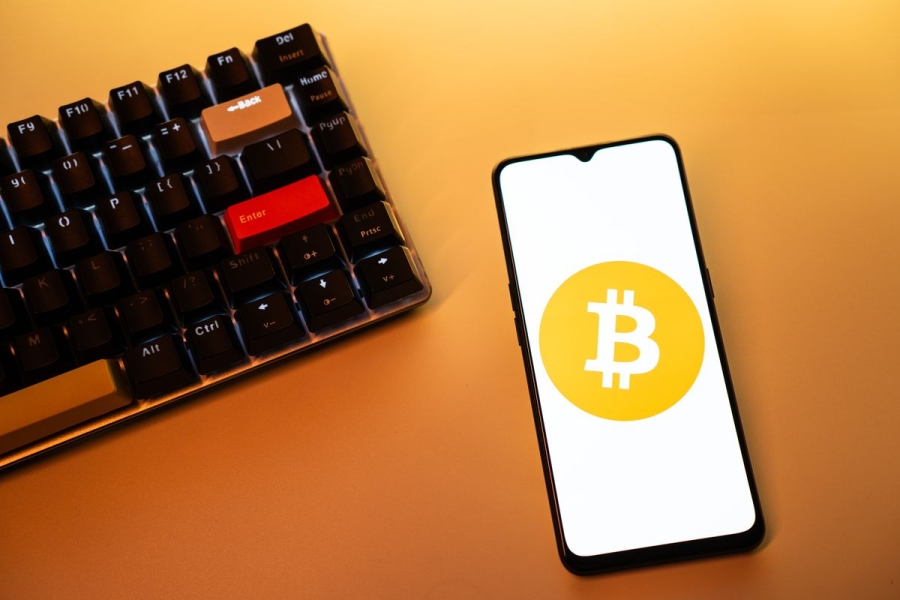 A mobile phone is displaying the logo of Bitcoin cryptocurrency on its screen next to a keyboard.