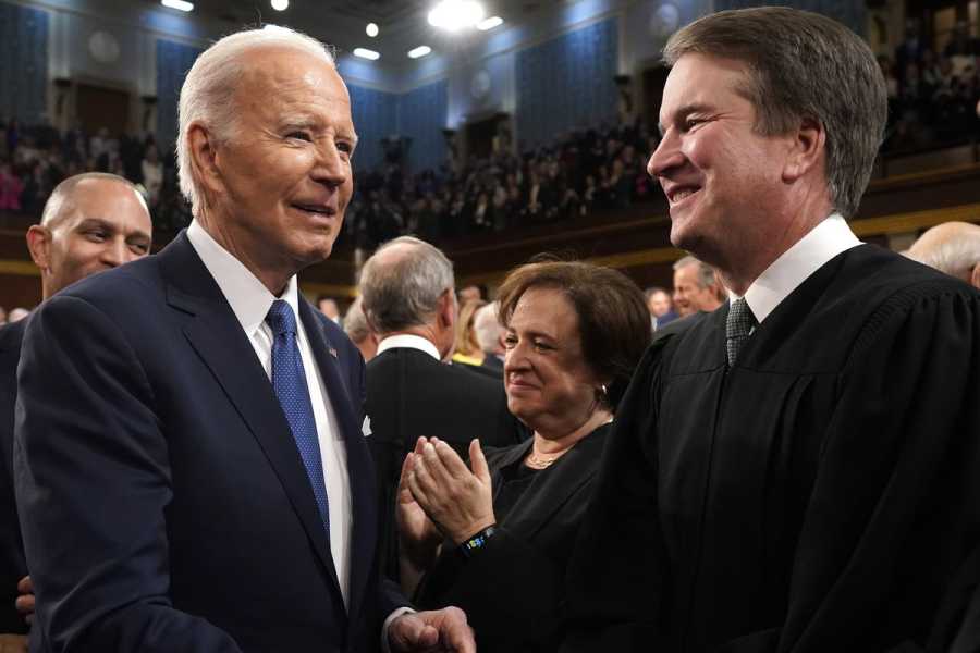 President Joe Biden and Justice Kavanaugh, both wearing suits, smile at each other.