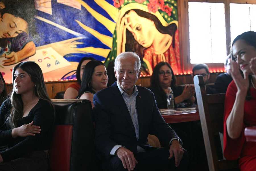 Joe Biden sits at a restaurant booth, surrounded by other diners. The wall behind them is painted with a vibrant mural.