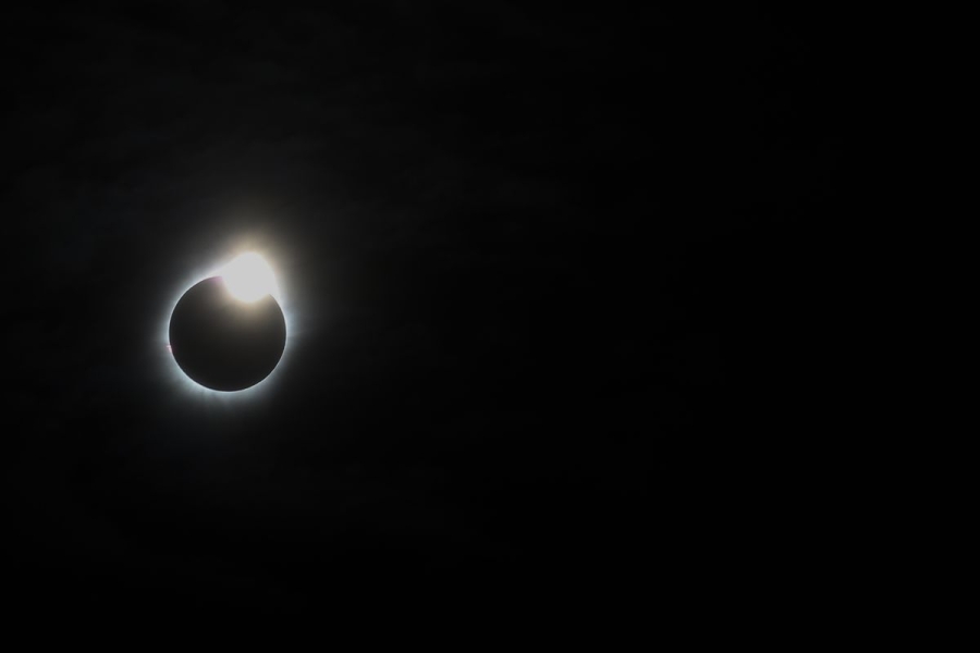 The eclipsed sun, a black circle surrounded by a glowing white corona, hangs in a black sky.