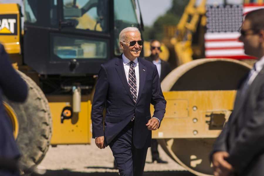 President Biden walks in front of a large construction machine.